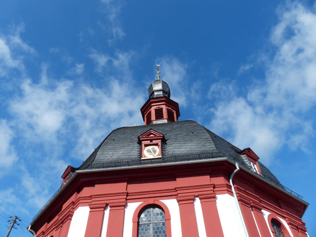 Außenbild der Kirche vor einem blauen Himmel mit Wolken. 