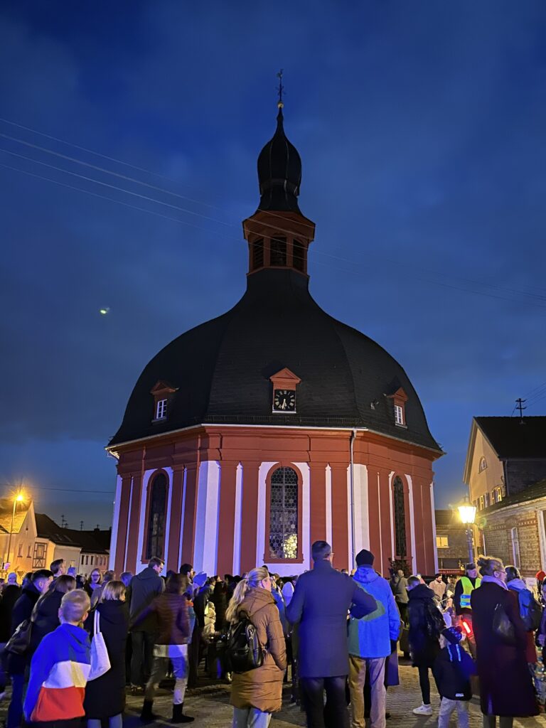 Beleuchtete Kirche von außen mit vielen Menschen davor