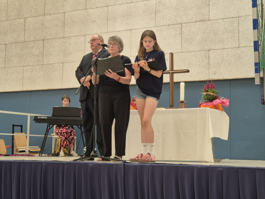 Martin Maurer, Christine Klaus und die Konfirmandin vor dem Altar auf der Bühne und im Hintergrund die Organistin.