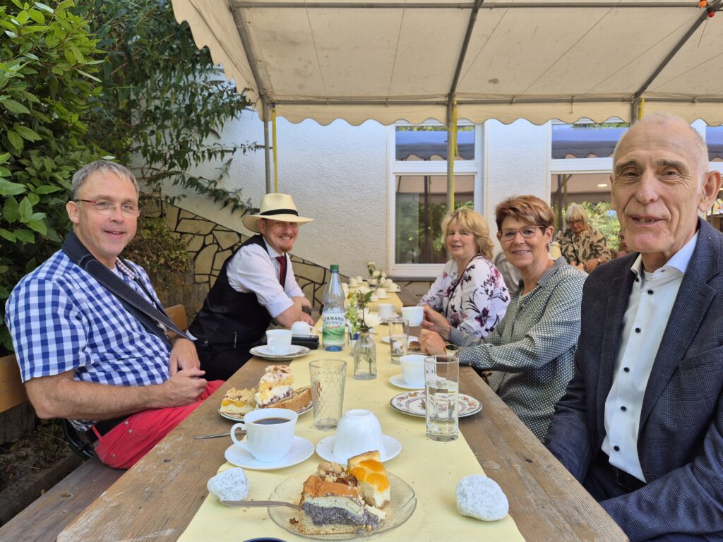 Menschen sitzen an Tischen und Bänken vor dem Gemeindehaus