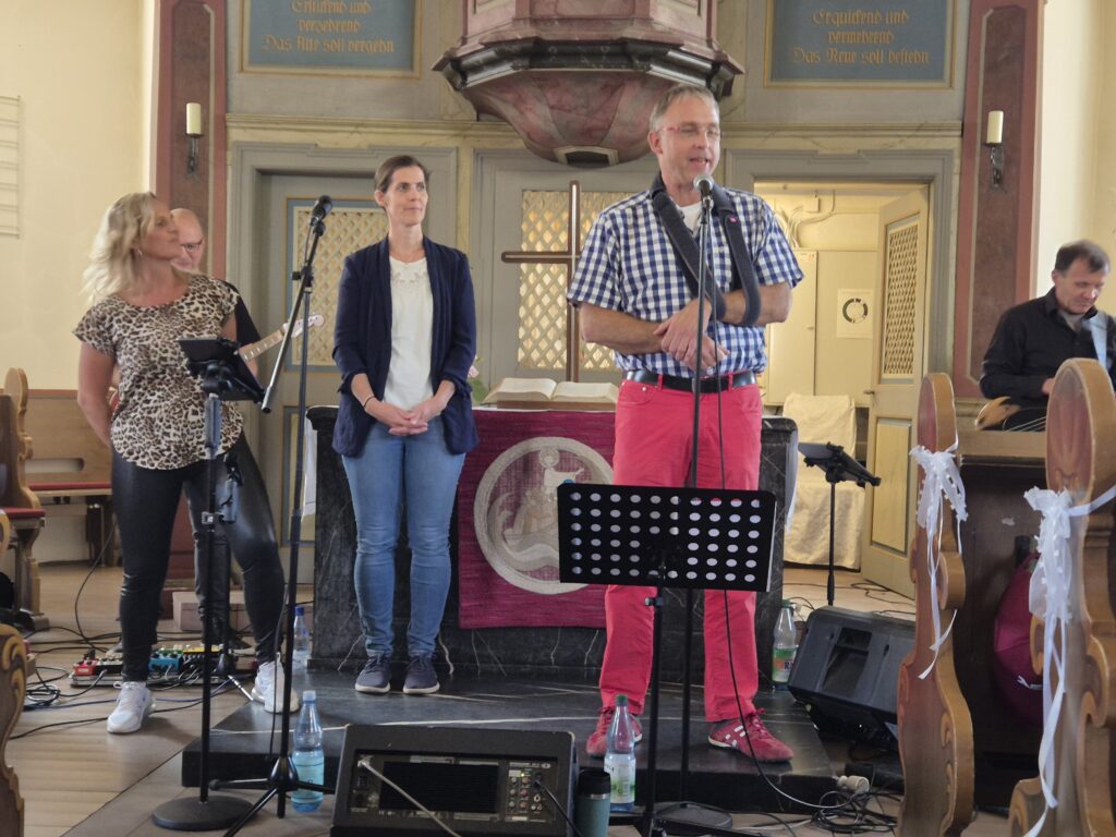 Pfarrer Tschöpel begrüßt Gäste und Band in der Kirche und steht vor dem Altar
