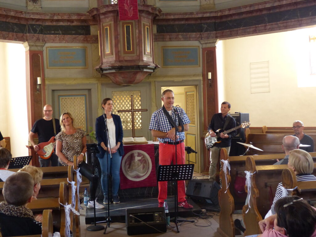 Pfarrer Tschöpel begrüßt Gäste und Band in der Kirche und steht vor dem Altar